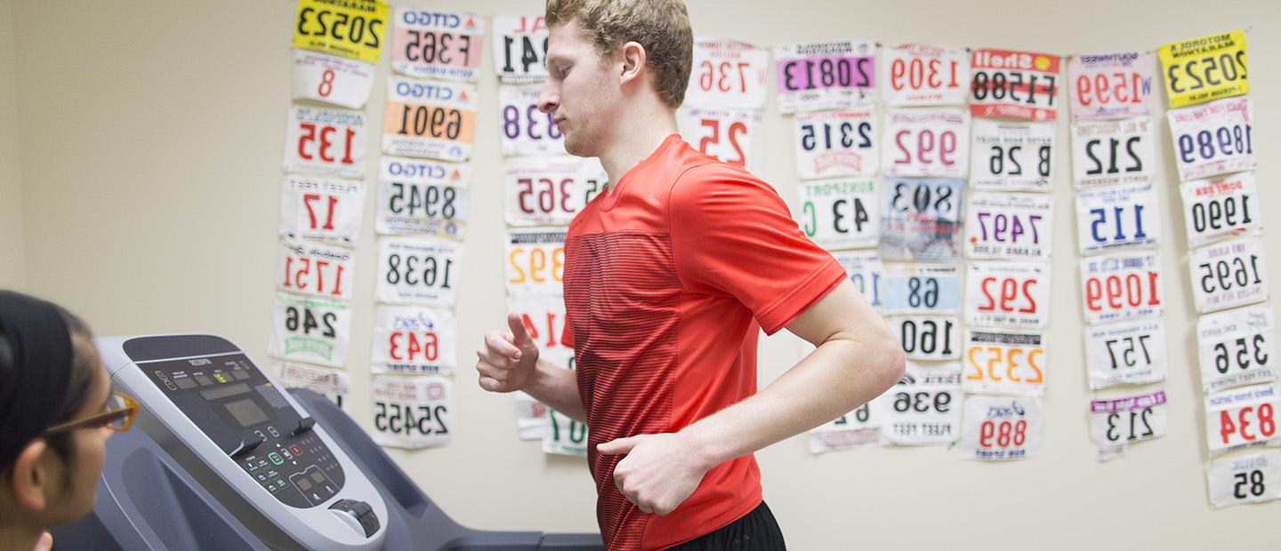 image of a person running on a treadmill with a second person monitoring the treadmill statistics